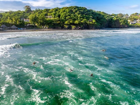 Surfers waiting offshore below Punta Mango's green headland