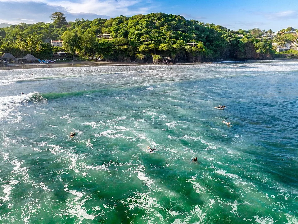 Surfers waiting offshore below the green headland at the separate eastern break of Punta Mango
